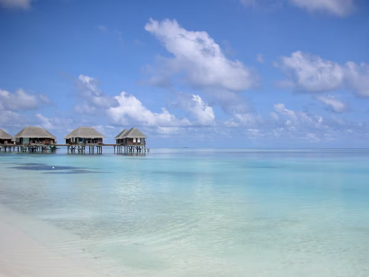 马尔代夫 Kani 岛地中海俱乐部（Club Med Kani）度假村的水上别墅，建在清澈碧绿的浅海泻湖上，蓝天白云下白色沙滩延伸至画面前景。