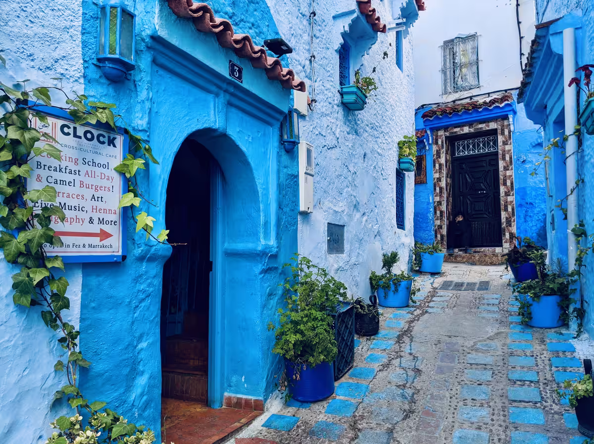 摩洛哥著名的“蓝色之城” - 舍夫沙万 （Chefchaouen) 一栋涂满鲜艳蓝色涂料的传统建筑入口，该建筑上挂着 Clock Cross-Cultural Cafe 的招牌。