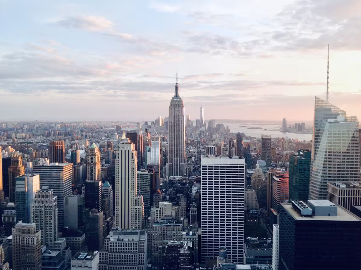纽约市曼哈顿天际线的鸟瞰全景，最突出的是黎明或黄昏柔和光线下的帝国大厦（Empire State Building）和更远处的世界贸易中心一号大楼（One World Trade Center）。