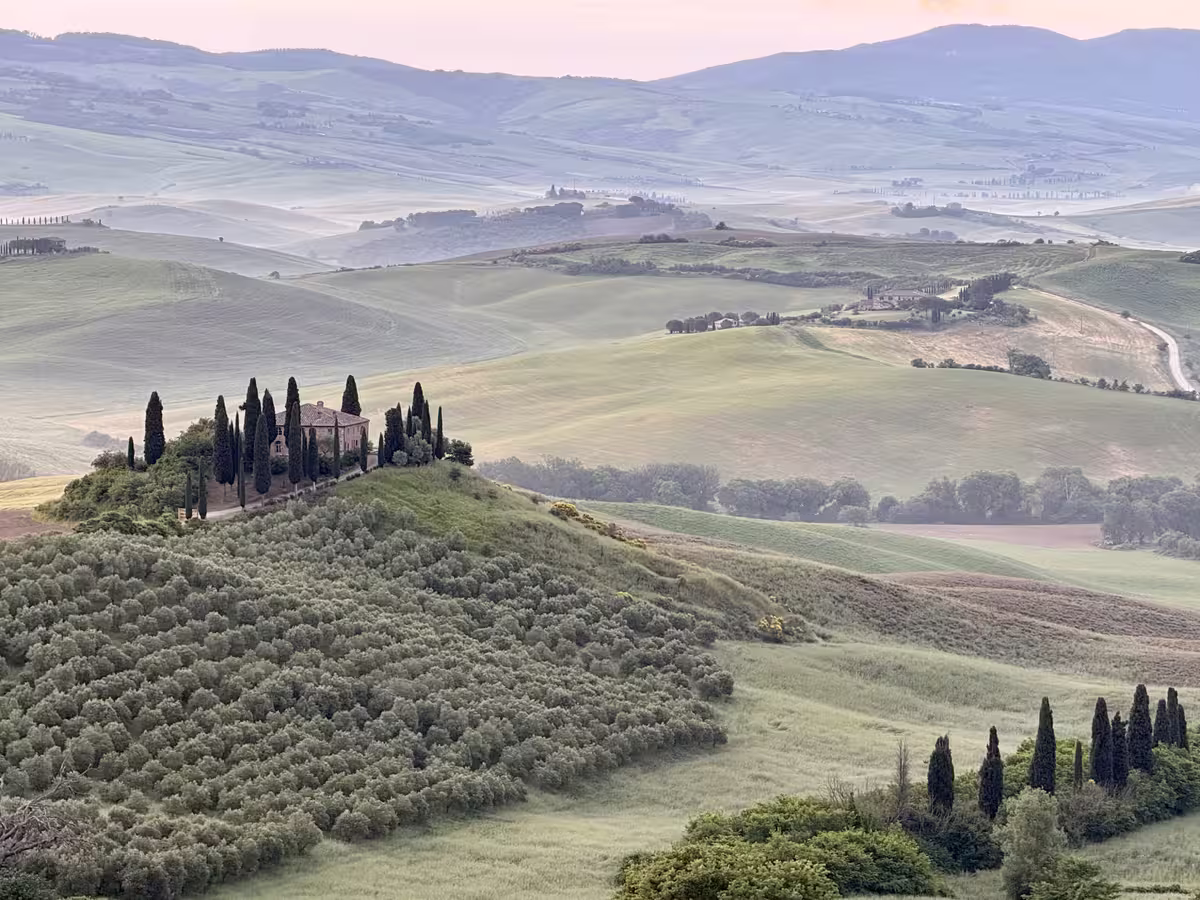 意大利托斯卡纳大区奥尔恰谷 (Val d'Orcia) 中著名的地标 - 贝尔维德雷农庄 (Podere Belvedere)，以其标志性的蜿蜒山丘和晨雾中的田园风光而闻名。